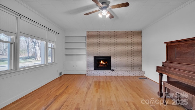 unfurnished living room with ceiling fan, a brick fireplace, built in features, light hardwood / wood-style floors, and ornamental molding