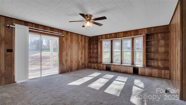 spare room featuring carpet flooring, ceiling fan, and wood walls