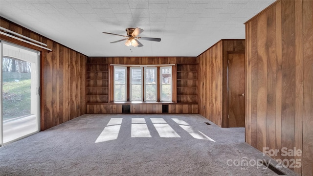 unfurnished room with ceiling fan, light carpet, and wooden walls