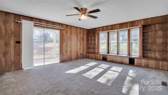 carpeted empty room with ceiling fan and wood walls