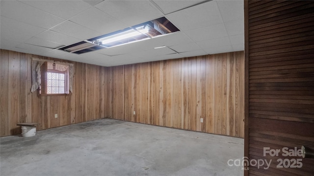 basement featuring a paneled ceiling and wooden walls