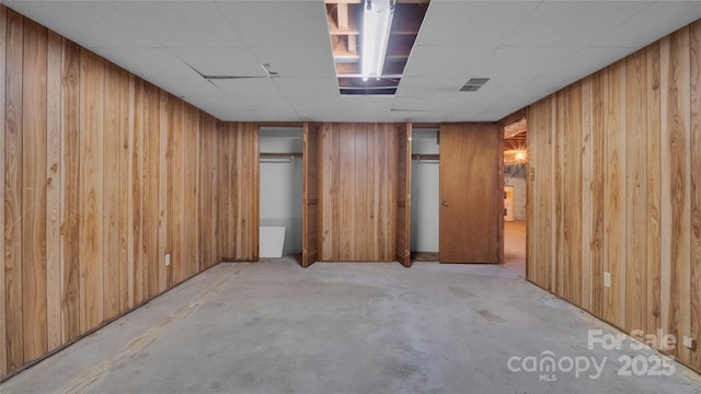 basement with a drop ceiling and wood walls