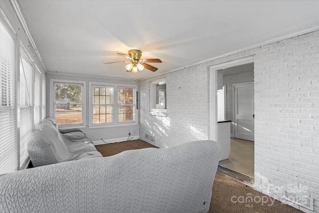 living room featuring ceiling fan, ornamental molding, brick wall, and dark carpet