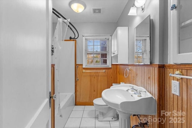 bathroom with tile patterned floors, wood walls, shower / tub combination, and toilet