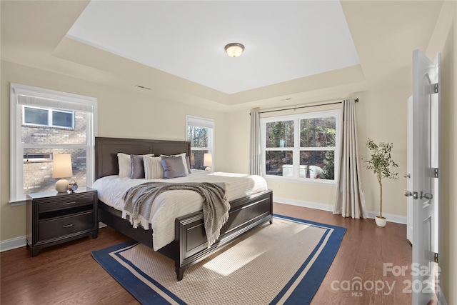 bedroom with dark hardwood / wood-style floors and a raised ceiling