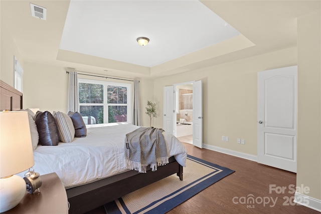 bedroom with a raised ceiling, dark hardwood / wood-style floors, and ensuite bathroom