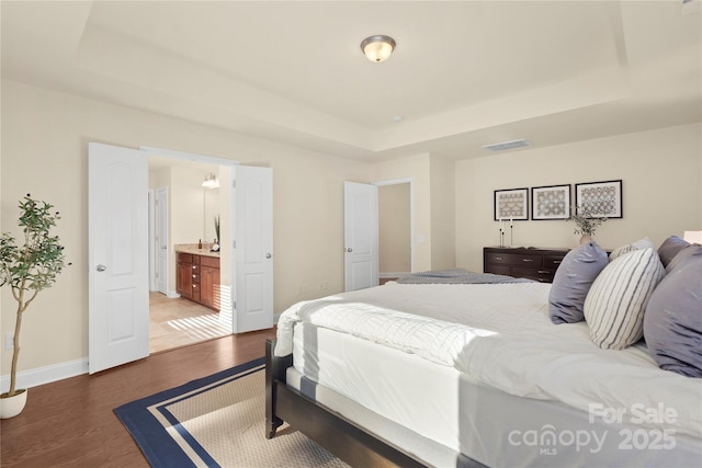 bedroom with connected bathroom, a raised ceiling, and hardwood / wood-style floors