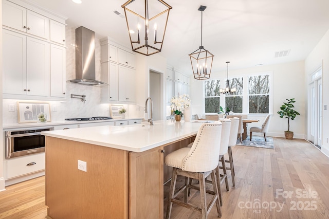 kitchen featuring a large island, white cabinetry, hanging light fixtures, wall chimney exhaust hood, and a chandelier