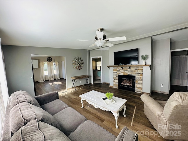 living room featuring dark hardwood / wood-style floors, a stone fireplace, and ceiling fan