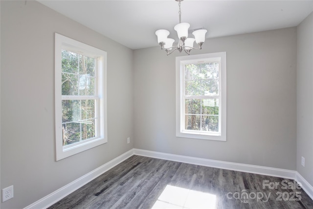 spare room featuring dark wood-type flooring and an inviting chandelier