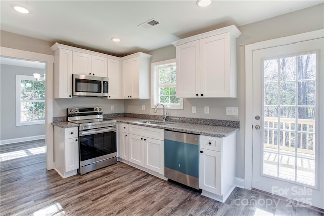 kitchen with stainless steel appliances, white cabinetry, sink, and light stone counters