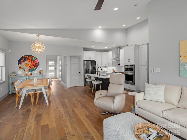 living room featuring sink, high vaulted ceiling, ceiling fan with notable chandelier, and light hardwood / wood-style flooring