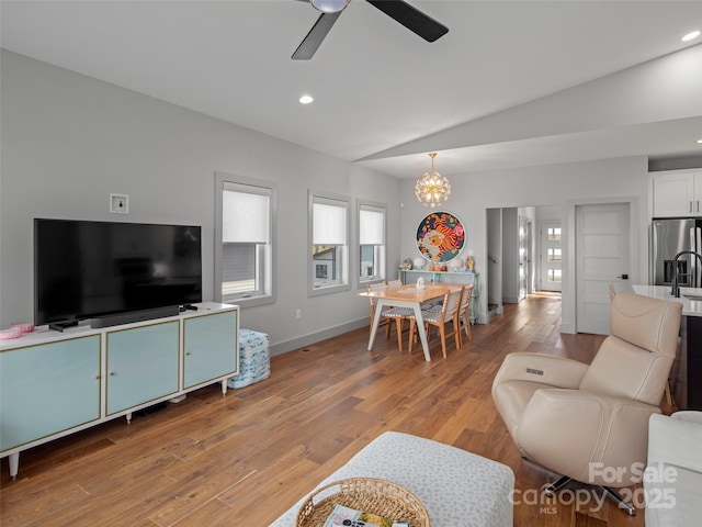 living room featuring ceiling fan with notable chandelier, vaulted ceiling, and light wood-type flooring