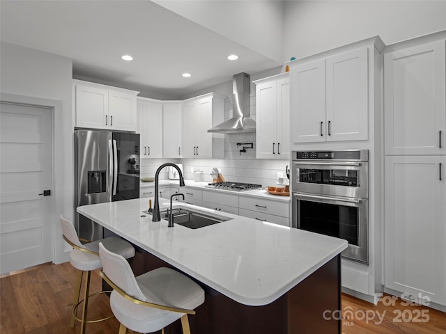 kitchen featuring white cabinets, stainless steel appliances, a kitchen island with sink, and wall chimney exhaust hood