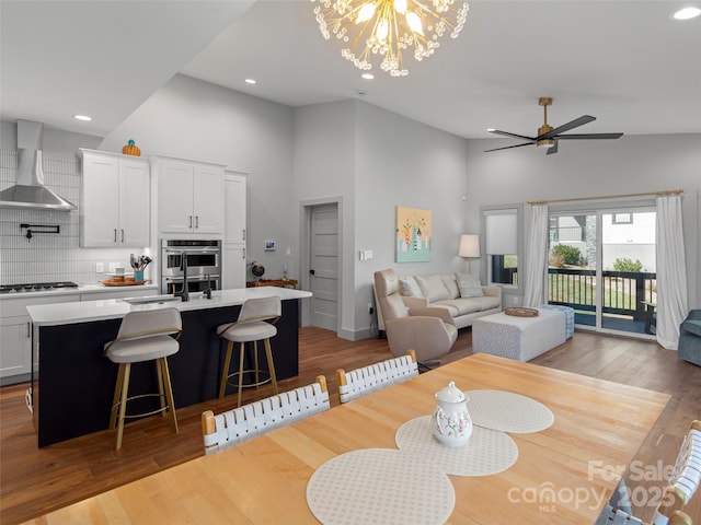 dining space featuring sink, ceiling fan with notable chandelier, light hardwood / wood-style floors, and a high ceiling