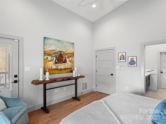 bedroom featuring ceiling fan, light hardwood / wood-style floors, high vaulted ceiling, and connected bathroom