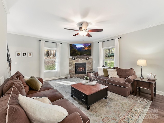 living room with a stone fireplace, crown molding, hardwood / wood-style floors, and ceiling fan