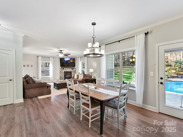 dining space featuring hardwood / wood-style floors, ceiling fan with notable chandelier, a stone fireplace, and crown molding