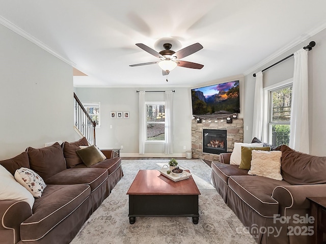 living room featuring a stone fireplace, ceiling fan, plenty of natural light, and ornamental molding