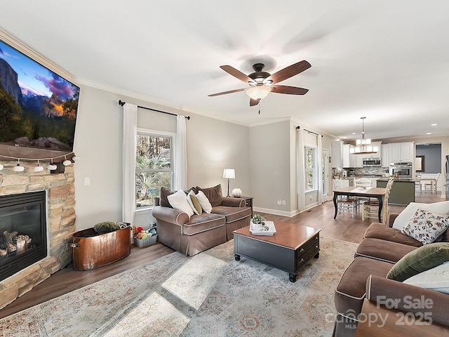 living room featuring ceiling fan with notable chandelier, crown molding, light wood-type flooring, and a fireplace