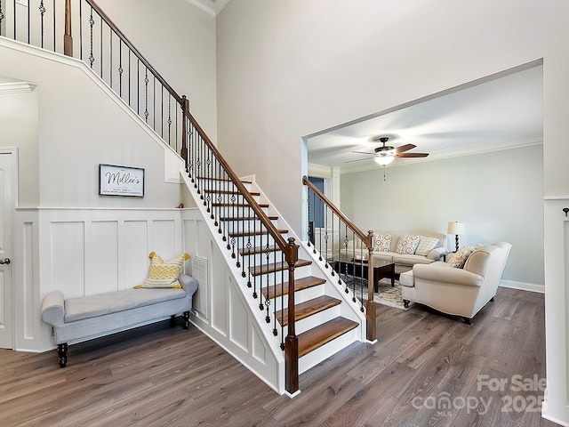 staircase featuring wood-type flooring, ceiling fan, and ornamental molding