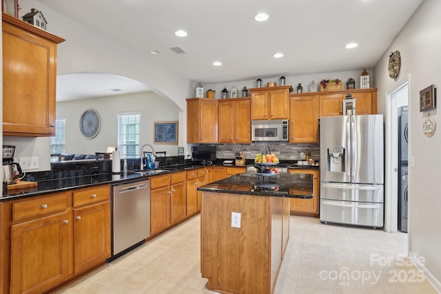 kitchen with sink, stainless steel appliances, kitchen peninsula, dark stone counters, and a kitchen island