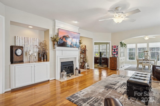 living room with a tiled fireplace, ceiling fan, and light hardwood / wood-style flooring