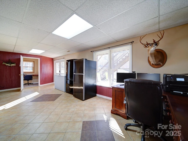 office featuring a drop ceiling, plenty of natural light, wooden walls, and light tile patterned flooring