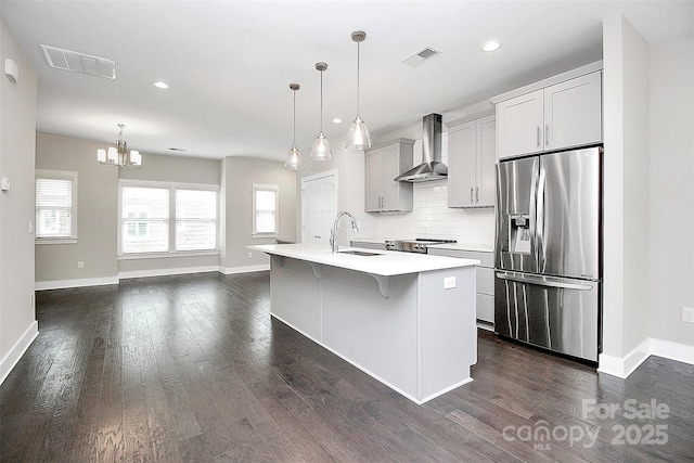 kitchen with appliances with stainless steel finishes, sink, wall chimney range hood, decorative light fixtures, and an island with sink