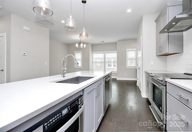 kitchen with pendant lighting, gray cabinetry, wall chimney range hood, sink, and stainless steel appliances