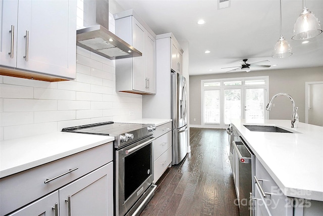 kitchen featuring sink, wall chimney range hood, tasteful backsplash, decorative light fixtures, and appliances with stainless steel finishes