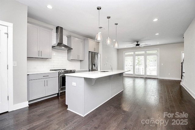 kitchen featuring gray cabinetry, sink, wall chimney exhaust hood, stainless steel appliances, and a kitchen island with sink