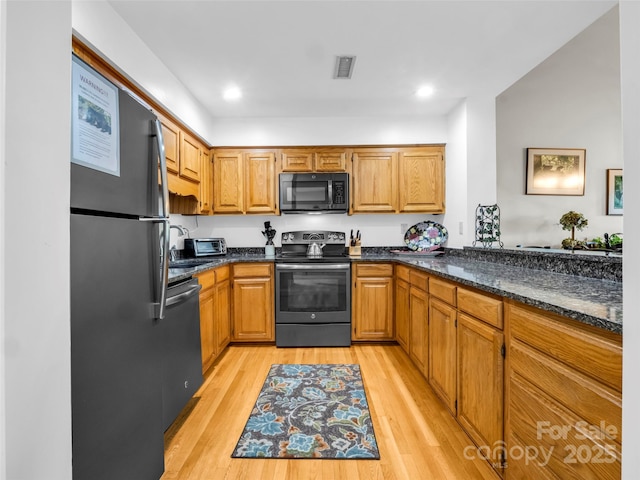 kitchen featuring sink, light hardwood / wood-style floors, dark stone counters, and black appliances