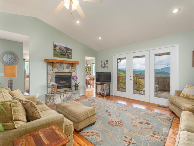 living room with french doors, vaulted ceiling, ceiling fan, light hardwood / wood-style flooring, and a stone fireplace