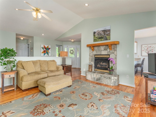 living room featuring a stone fireplace, ceiling fan, lofted ceiling, and hardwood / wood-style flooring