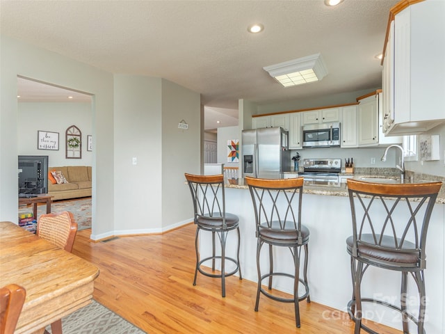 kitchen with kitchen peninsula, appliances with stainless steel finishes, a textured ceiling, sink, and white cabinets