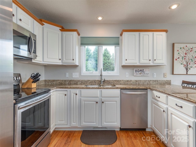 kitchen with stainless steel appliances, sink, stone counters, white cabinets, and light hardwood / wood-style floors