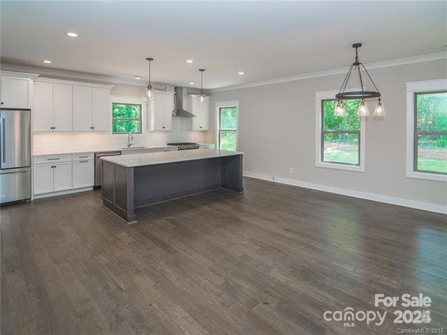 kitchen featuring stainless steel appliances, wall chimney range hood, decorative light fixtures, a center island, and white cabinetry