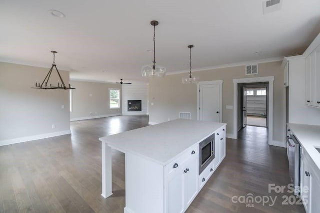 kitchen featuring white cabinetry, stainless steel microwave, ceiling fan, pendant lighting, and a kitchen island