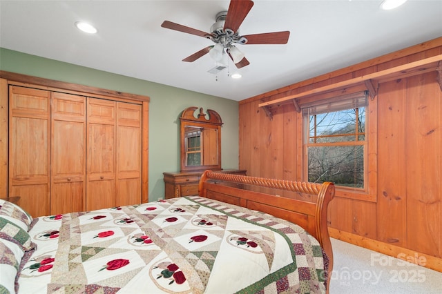 carpeted bedroom with a closet, ceiling fan, and wood walls