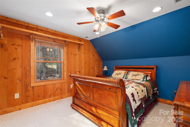 carpeted bedroom with vaulted ceiling, ceiling fan, and wood walls