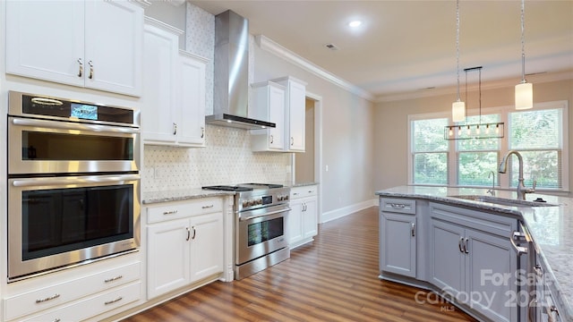 kitchen with sink, wall chimney exhaust hood, light stone countertops, white cabinetry, and stainless steel appliances