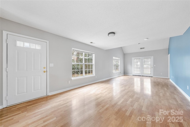 foyer entrance featuring lofted ceiling, a textured ceiling, and light wood-type flooring