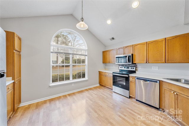 kitchen featuring vaulted ceiling, appliances with stainless steel finishes, pendant lighting, and light hardwood / wood-style flooring