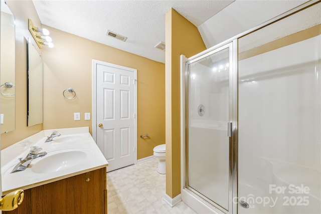 bathroom with vanity, toilet, a shower with shower door, and a textured ceiling