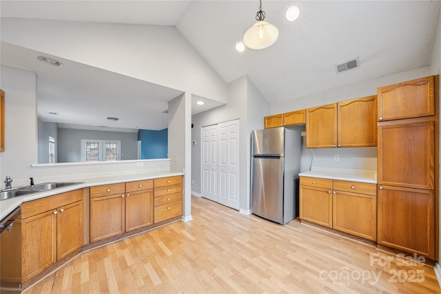 kitchen featuring sink, vaulted ceiling, hanging light fixtures, light hardwood / wood-style flooring, and appliances with stainless steel finishes