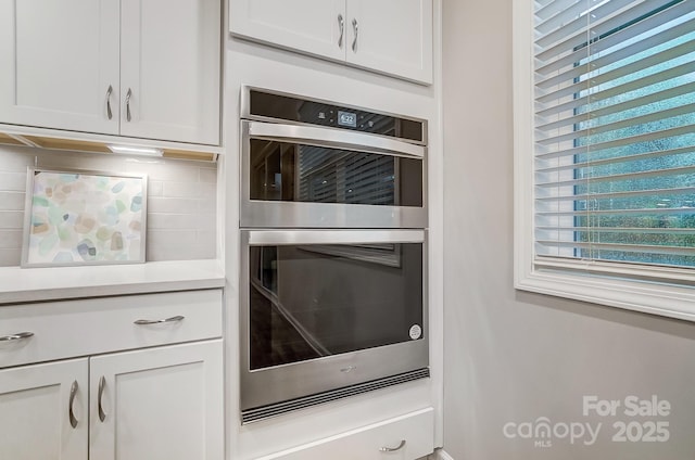 kitchen with decorative backsplash, white cabinets, and stainless steel double oven