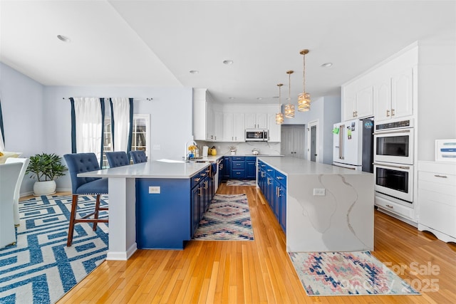 kitchen with white appliances, white cabinets, light hardwood / wood-style floors, hanging light fixtures, and blue cabinets