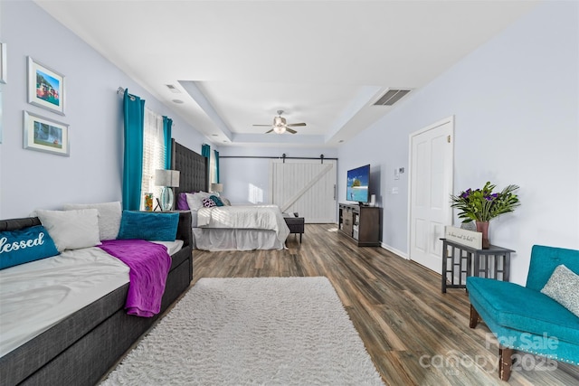 bedroom featuring ceiling fan, dark wood-type flooring, a tray ceiling, and a barn door