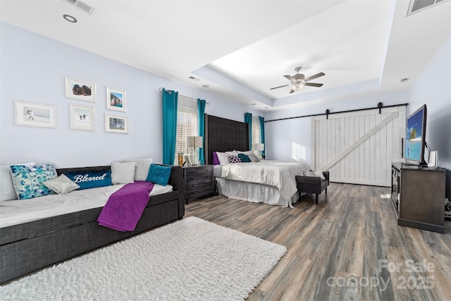 bedroom featuring ceiling fan, a barn door, dark hardwood / wood-style flooring, and a tray ceiling